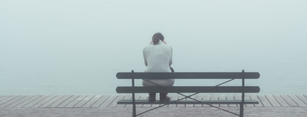 Eine Frau sitzt verzweifelt auf einer Bank im Nebel.
